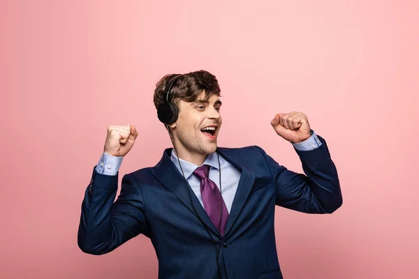 Empresário animado dançando enquanto ouve música em fones de ouvido em fundo rosa — Fotografia de Stock