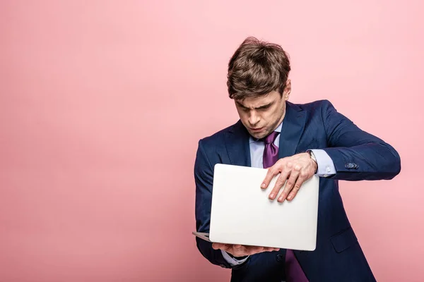 Seriöser Geschäftsmann im Anzug öffnet Laptop auf rosa Hintergrund — Stockfoto