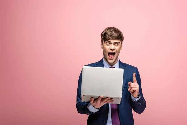 Aufgeregter Geschäftsmann zeigt Idee-Geste, während er Laptop auf rosa Hintergrund hält — Stockfoto