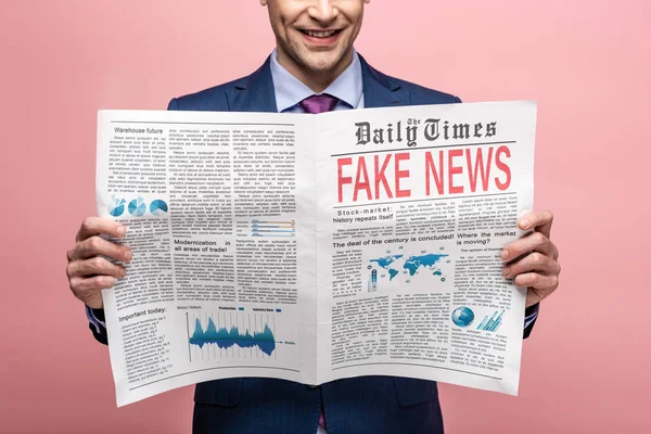 Cropped view of businessman reading newspaper with fake news isolated on pink — Stock Photo