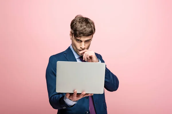 Thoughtful businessman using smartphone while hoding hand near face on pink background — Stock Photo