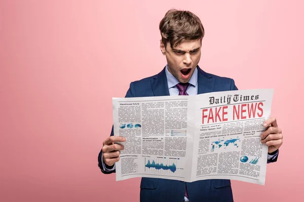 Geschockter Geschäftsmann liest Zeitung mit Fake News auf rosa Hintergrund — Stockfoto