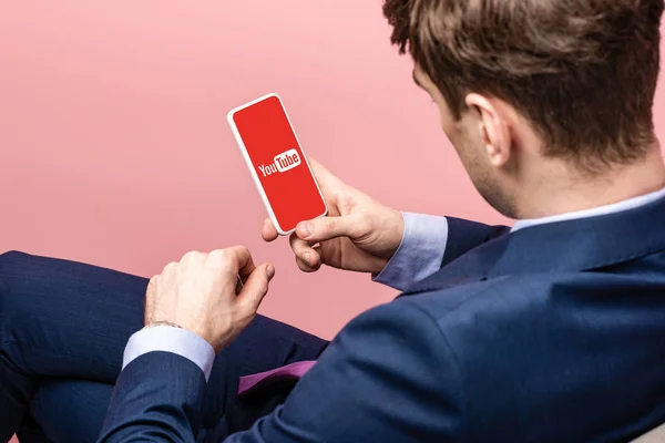 KYIV, UCRAINA - 16 MAGGIO 2019: vista ritagliata dell'uomo d'affari utilizzando lo smartphone con l'app youtube, isolato su rosa — Foto stock