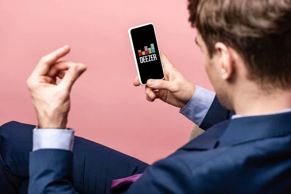 KYIV, UCRANIA - 16 DE MAYO DE 2019: vista recortada del hombre de negocios utilizando el teléfono inteligente con aplicación deezer, aislado en rosa - foto de stock