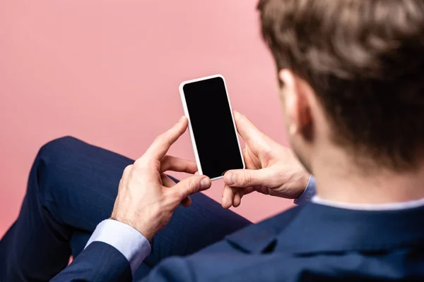 Rückseite des Geschäftsmannes sitzt und hält Smartphone mit leerem Bildschirm isoliert auf rosa — Stockfoto