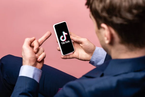 KYIV, UKRAINE - MAY 16, 2019: cropped view of businessman using smartphone with Tik Tok app and showing middle finger, isolated on pink — Stock Photo