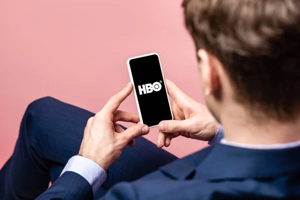 KYIV, UCRANIA - 16 DE MAYO DE 2019: vista recortada del hombre de negocios utilizando el teléfono inteligente con la aplicación HBO, aislado en rosa - foto de stock