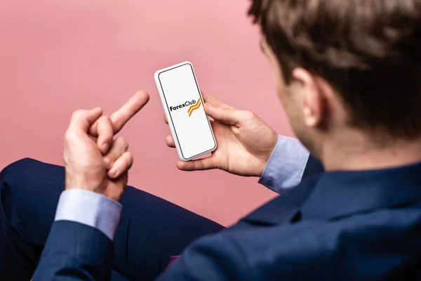 KYIV, UKRAINE - MAY 16, 2019: cropped view of businessman using smartphone with forex club app and showing middle finger, isolated on pink — Stock Photo
