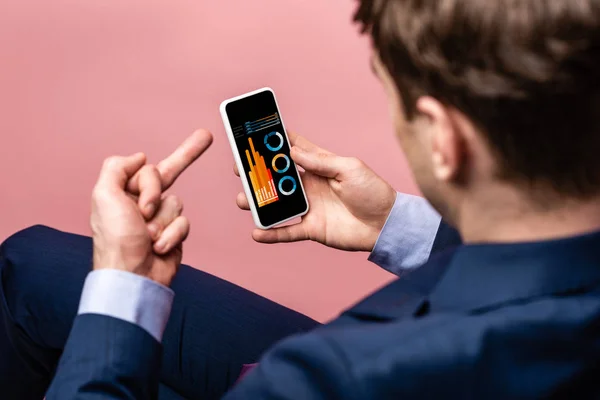 Vista cortada de empresário usando smartphone com infográfico ao mostrar o dedo médio, isolado em rosa — Fotografia de Stock