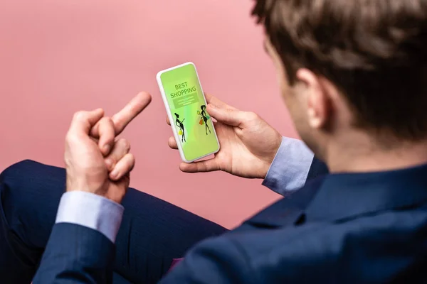 Vista cortada de homem de negócios usando smartphone com melhor aplicativo de compras ao mostrar o dedo médio, isolado em rosa — Fotografia de Stock
