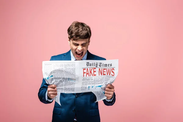 Angry businessman screaming while reading newspaper with fake news isolated on pink — Stock Photo