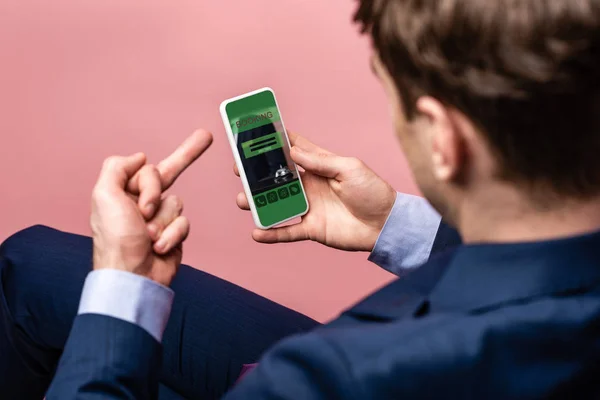 Cropped view of businessman using smartphone with booking app while showing middle finger, isolated on pink — Stock Photo