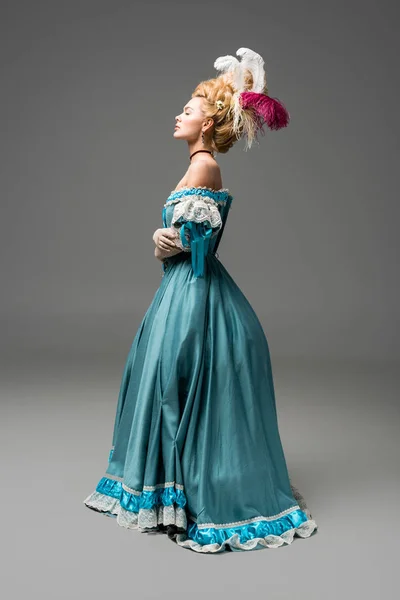 Side view of pompous victorian woman in wig standing in blue dress on grey — Stock Photo
