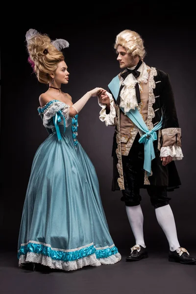 Handsome victorian man and woman in wigs standing and holding hands on black — Stock Photo