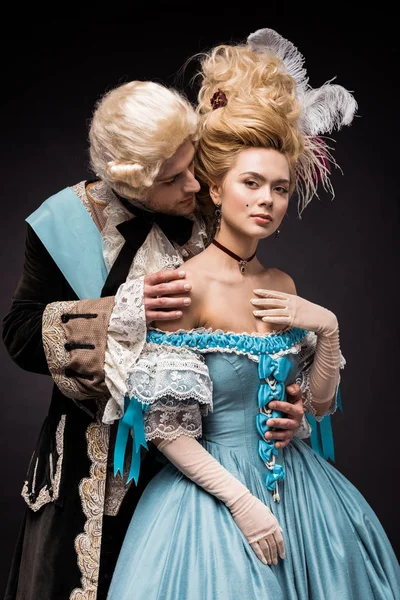 Handsome victorian man looking at young beautiful woman in wig on black — Stock Photo