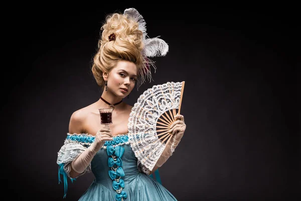 Attractive victorian woman holding fan and wine glass on black — Stock Photo