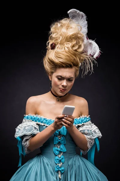 Attraente giovane donna vittoriana in abito blu utilizzando smartphone mentre mostra la lingua sul nero — Foto stock