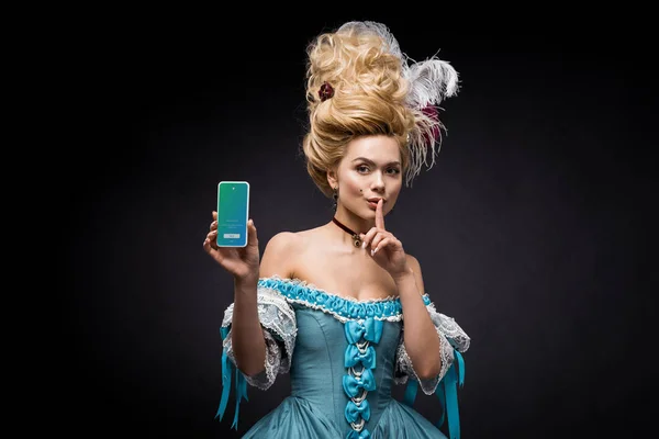 KYIV, UKRAINE - JUNE 5, 2019: attractive victorian woman holding smartphone with twitter app on screen and showing hush sign on black — Stock Photo