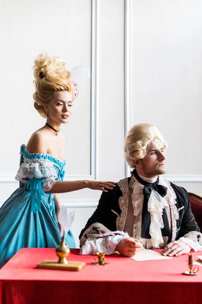 Selective focus of victorian woman in wig standing near pompous man holding feather — Stock Photo