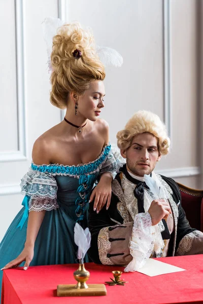 Selective focus of victorian girl in wig standing near handsome pompous man holding feather near paper — Stock Photo