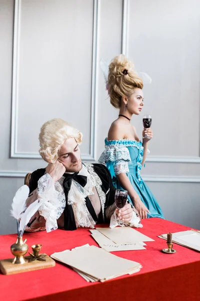 Sad victorian man in wig holding glass wine near pompous woman — Stock Photo