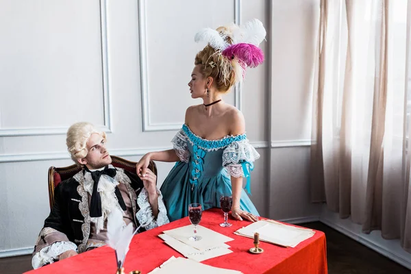 Handsome victorian man in wig holding hands with pompous woman near wine glasses — Stock Photo