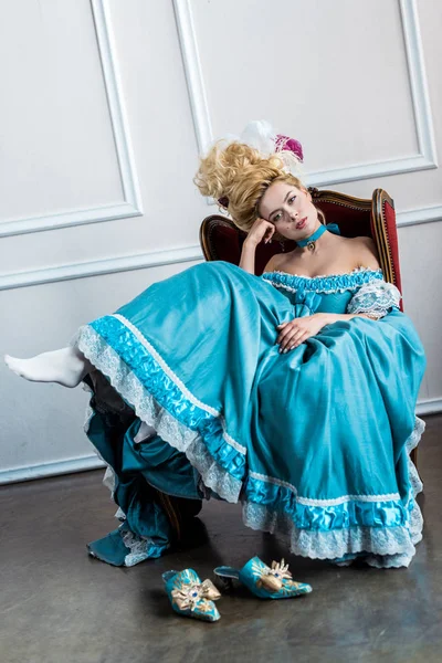 Mujer victoriana aburrida en peluca con plumas sentadas en silla antigua - foto de stock