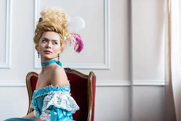 Beautiful victorian woman in wig with feathers sitting on antique chair — Stock Photo