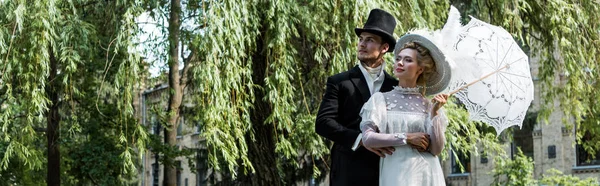 Panoramic shot of handsome victorian man standing with woman holding umbrella — Stock Photo