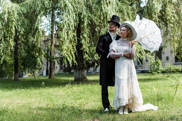 Guapo victoriano hombre de pie con mujer sosteniendo paraguas - foto de stock
