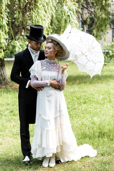 Handsome victorian man standing with attractive woman holding umbrella — Stock Photo