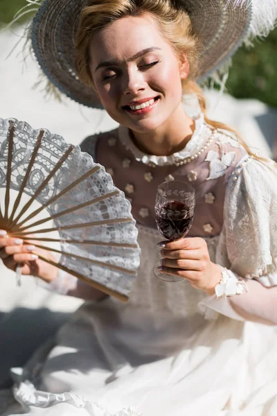 Щаслива молода вікторіанка з закритими очима тримає вентилятор і келих для вина — стокове фото
