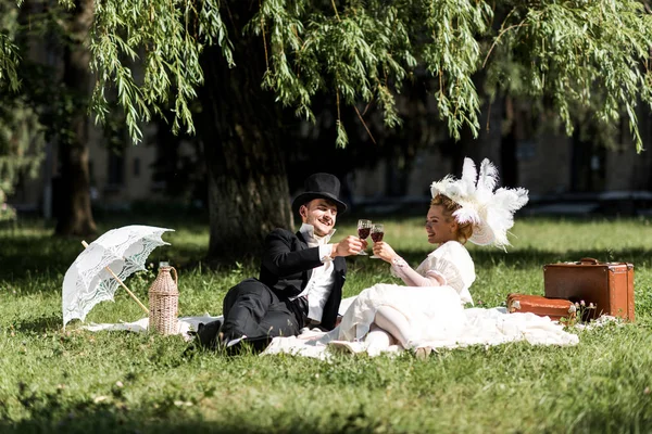 Happy man and woman siting on blanket and clinking wine glasses — Stock Photo