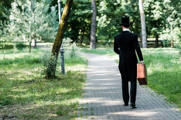 Back view of victorian man in hat holding baggage and walking outside — Stock Photo