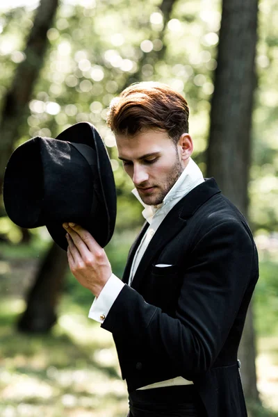 Guapo aristocrático hombre sosteniendo sombrero mientras está de pie en traje - foto de stock