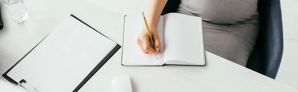 Vista ritagliata della donna incinta scrivere note sul tavolo bianco — Foto stock