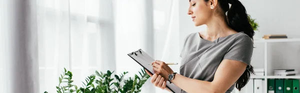 Plano panorámico de la mujer embarazada tomando notas en el cuaderno en la oficina - foto de stock