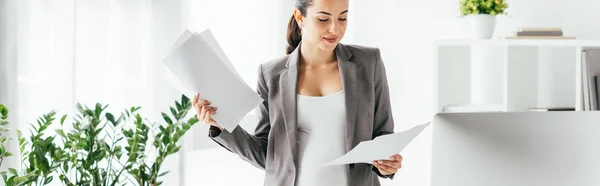 Plano panorámico de la mujer embarazada leyendo papeles mientras está de pie en la oficina - foto de stock