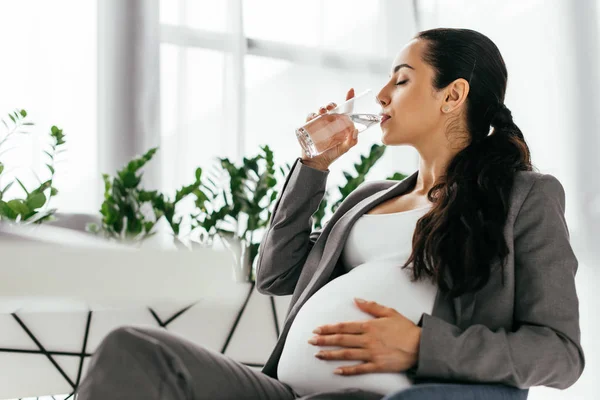 Pregnant woman sitting in office chair and drinking water — Stock Photo