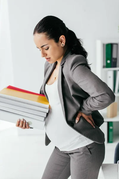 Mujer embarazada sosteniendo carpetas y agarrado en la parte posterior — Stock Photo