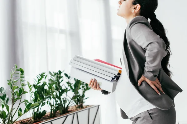 Pregnant woman holding back while standing with many folders — Stock Photo