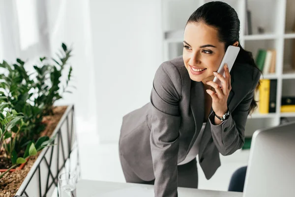 Donna incinta magra sul tavolo mentre parla sullo smartphone e distoglie lo sguardo — Foto stock