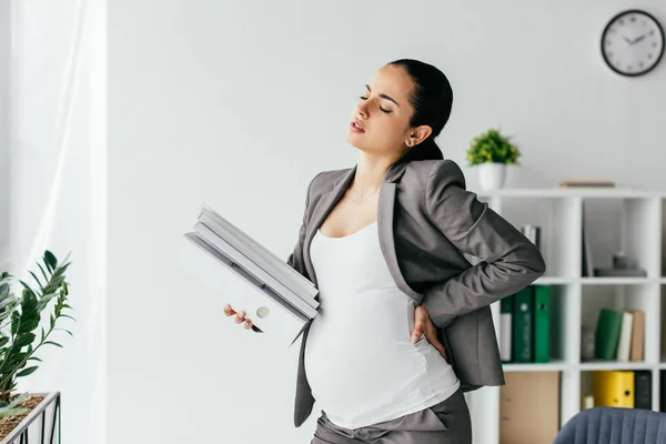 Exhausted pregnant woman holding back and plenty of folders — Stock Photo