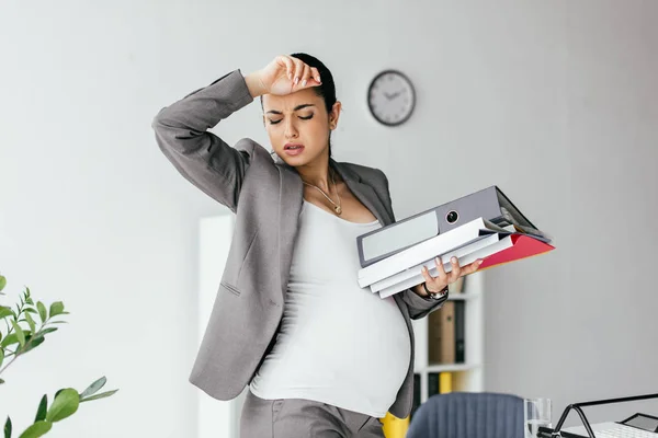 Exhausted pregnant woman enduring pain and holding folders — Stock Photo