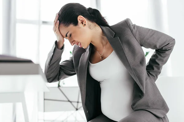 Femme enceinte tenant la tête avec la main à cause de la douleur — Photo de stock