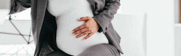 Panoramic shot of pregnant woman holding her belly and sitting behind table — Stock Photo