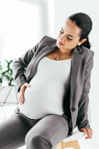 Pregnant woman sitting in office chair and touching belly — Stock Photo