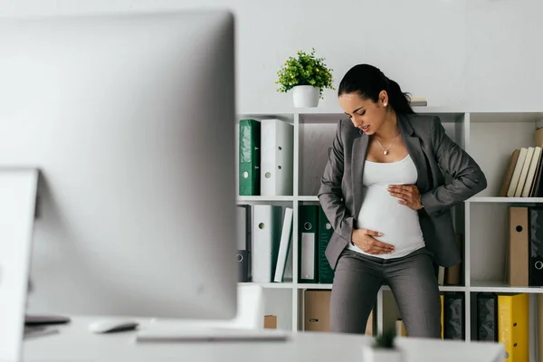 Angespannte Schwangere steht neben Bücherregal und hält Bauch — Stockfoto