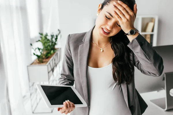 Donna incinta che tiene la compressa digitale e tocca la fronte con mano a causa del dolore — Foto stock