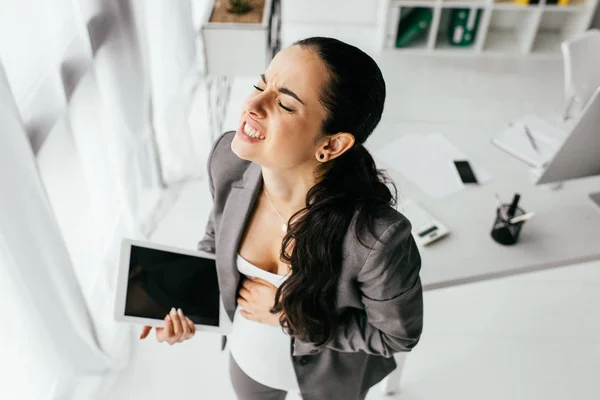 High angle view of pregnant woman holding digital tablet and making grimace because of pain — Stock Photo
